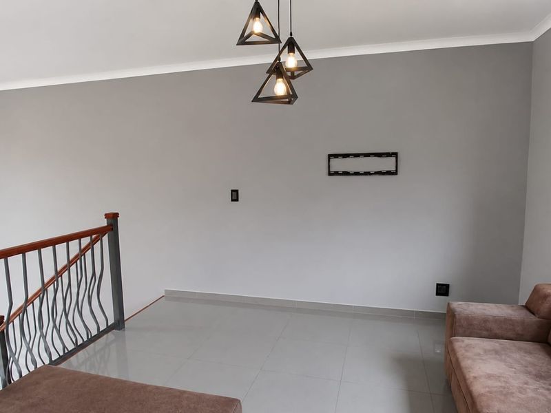A bright living area featuring neutral grey walls, polished tile flooring, and a decorative metal staircase railing with wooden handrail.