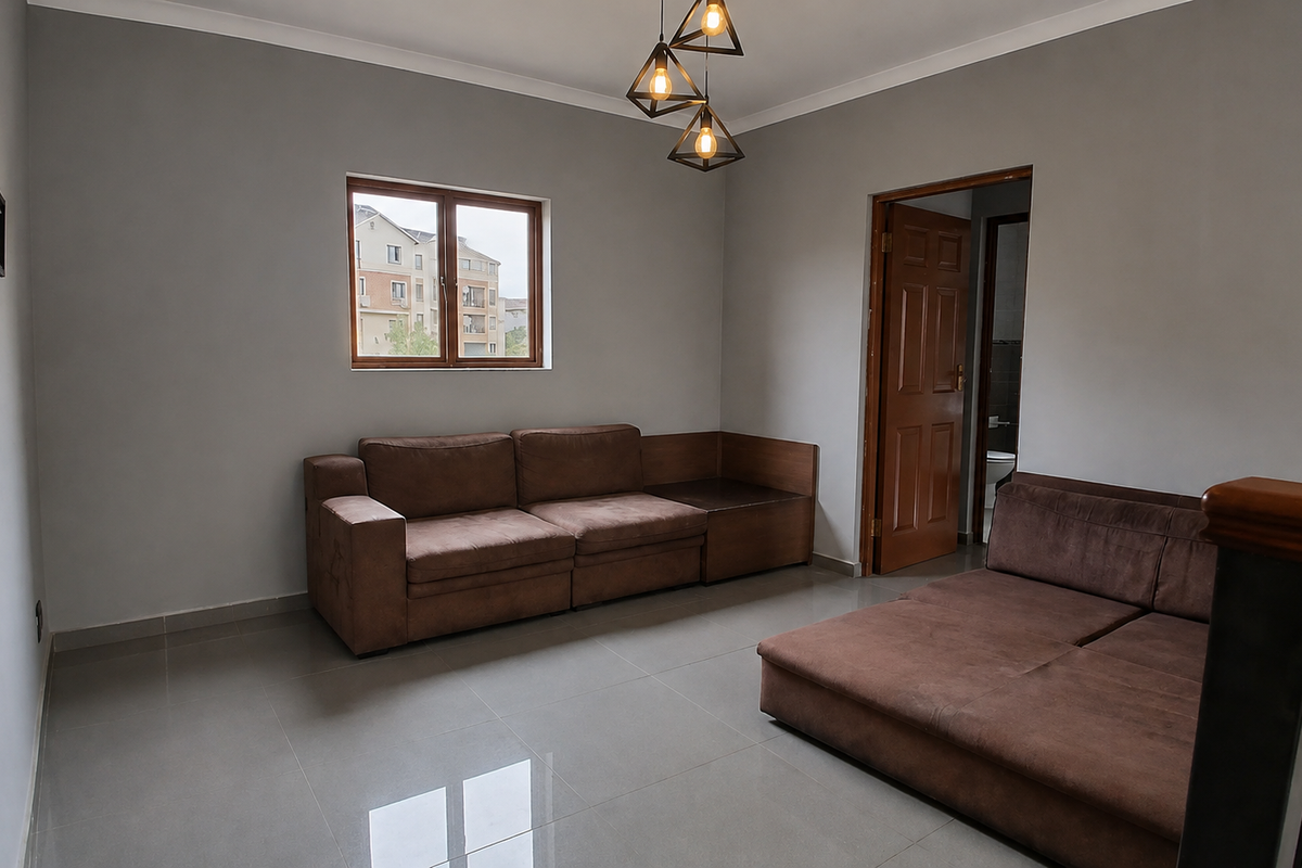 A living room featuring neutral grey walls, large format floor tiles, modern geometric pendant lighting, and a wooden door leading to an adjacent room.