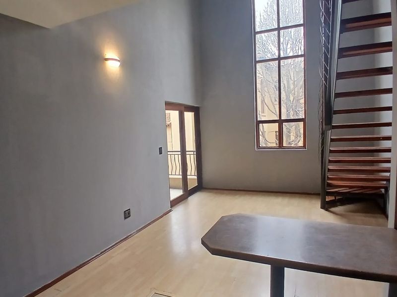 Spacious open-plan living area featuring double-volume ceilings, a modern spiral staircase, large windows for natural light, and access to a private balcony.