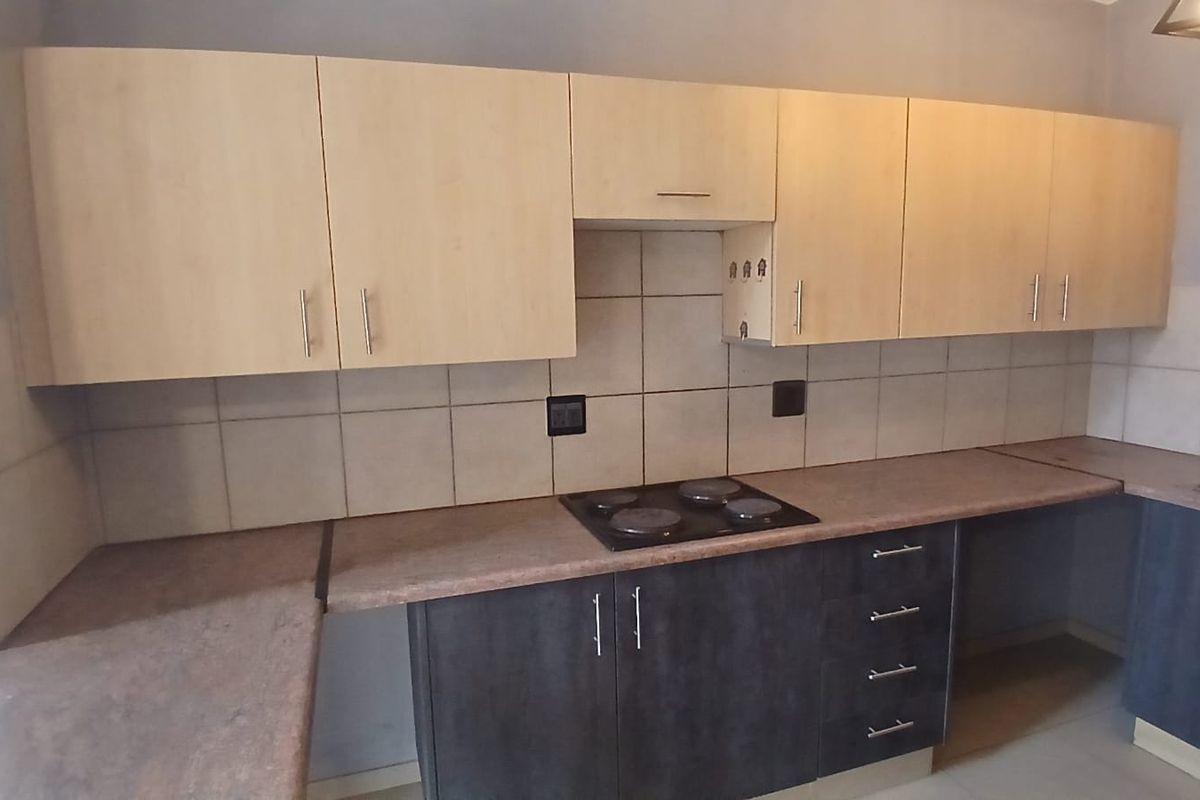 A functional kitchen featuring two-tone cabinetry, laminate countertops, a built-in electric hob, and a tiled backsplash.