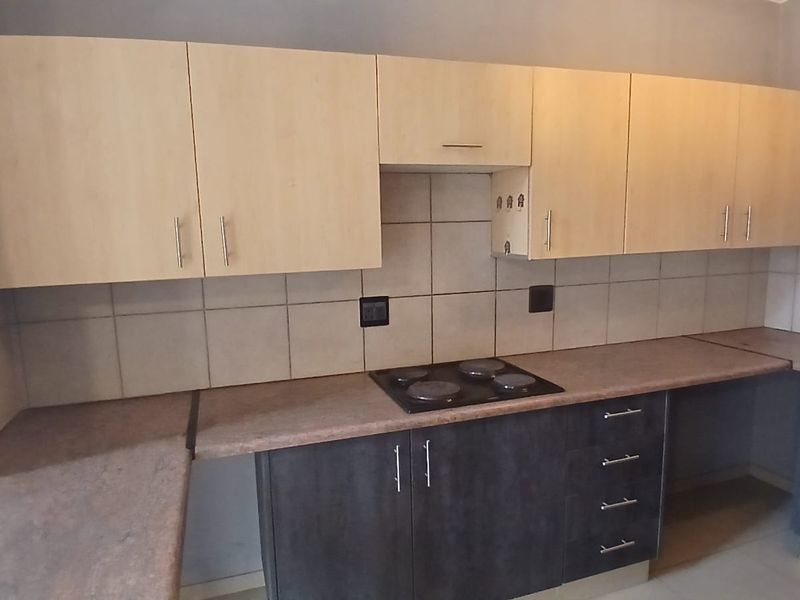 A functional kitchen featuring two-tone cabinetry, laminate countertops, a built-in electric hob, and a tiled backsplash.