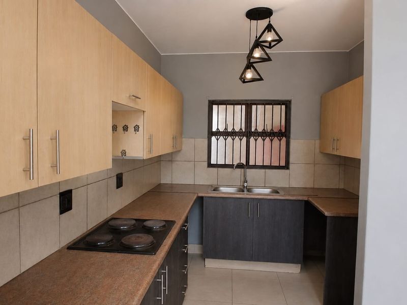 A functional kitchen featuring light wood upper cabinets, dark lower cabinetry, laminate countertops, an electric hob, and a stainless steel sink with tiled backsplash.
