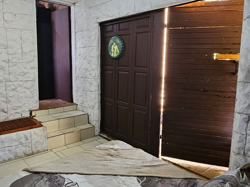 A bedroom featuring textured stone-effect wall finishes, tiled steps leading to an adjacent area, and a timber door opening to the exterior.