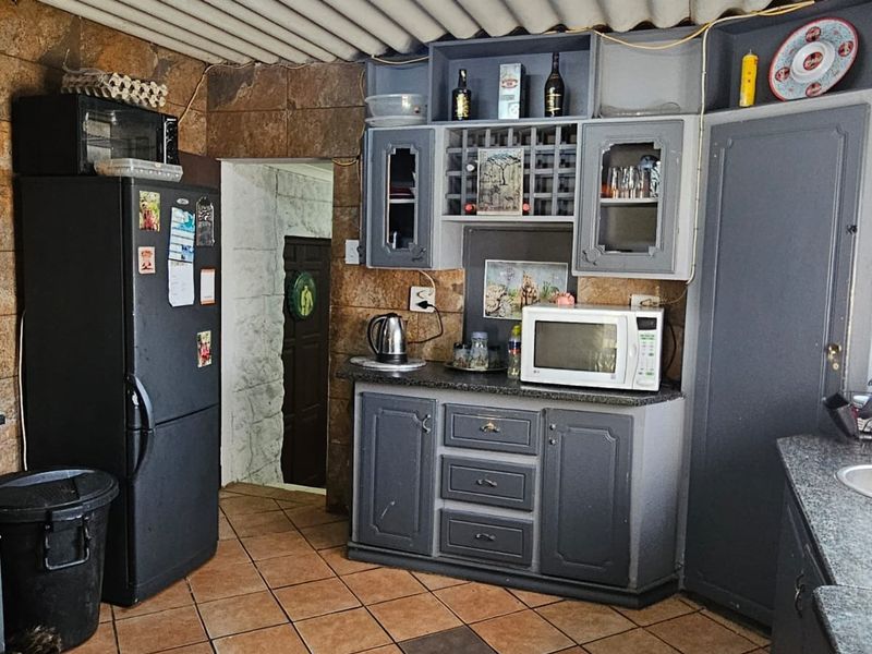 A rustic kitchen featuring stone wall cladding, tiled flooring, fitted cabinetry with granite countertops, and a corrugated ceiling finish.