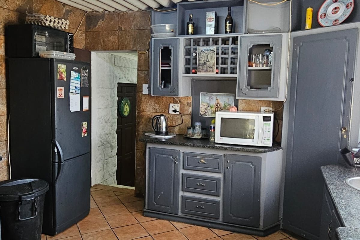A rustic kitchen featuring stone wall cladding, tiled flooring, fitted cabinetry with granite countertops, and a corrugated ceiling finish.
