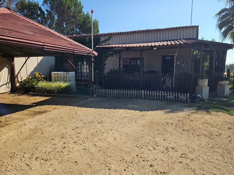 Rear view of the farm property featuring a covered patio area, stone-clad exterior walls, and a metal roof structure set against a natural landscape.