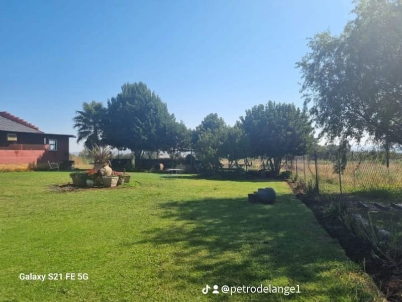 A spacious, well-maintained garden area featuring a lush lawn, mature trees, and perimeter chain-link fencing on a farm property.