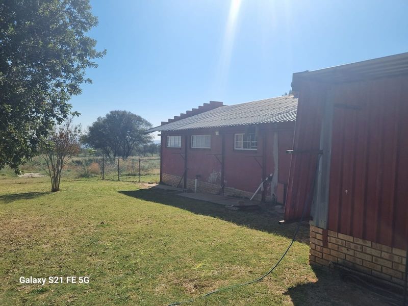 Rear view of a farm building featuring a corrugated metal roof, brick construction, and surrounding garden area.
