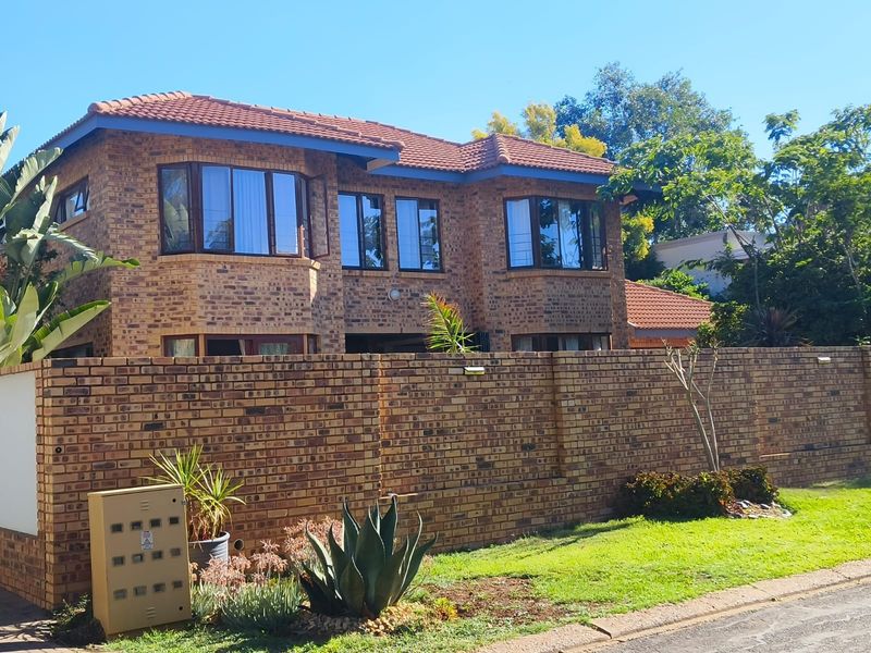 A double-story face brick house featuring bay windows, a tiled roof, and a secure perimeter brick wall with an integrated electrical box.