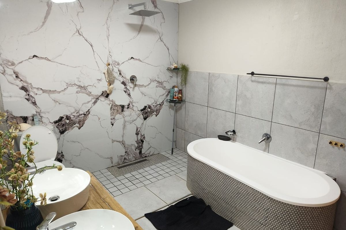 Modern bathroom featuring a freestanding bathtub, walk-in shower with rainfall head, and a double vanity with marble-look wall tiling.