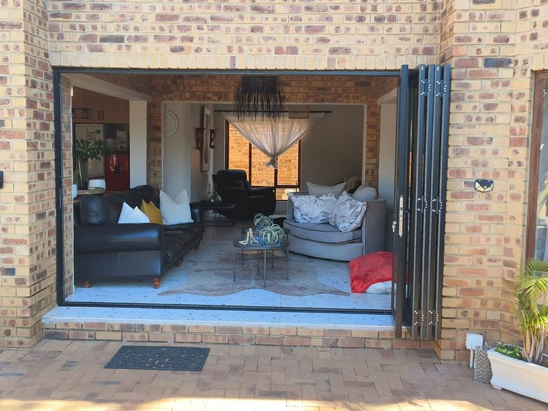 A seamless transition from the paved patio to the interior living space through large black-framed bi-fold doors, featuring exposed brickwork and tiled flooring.