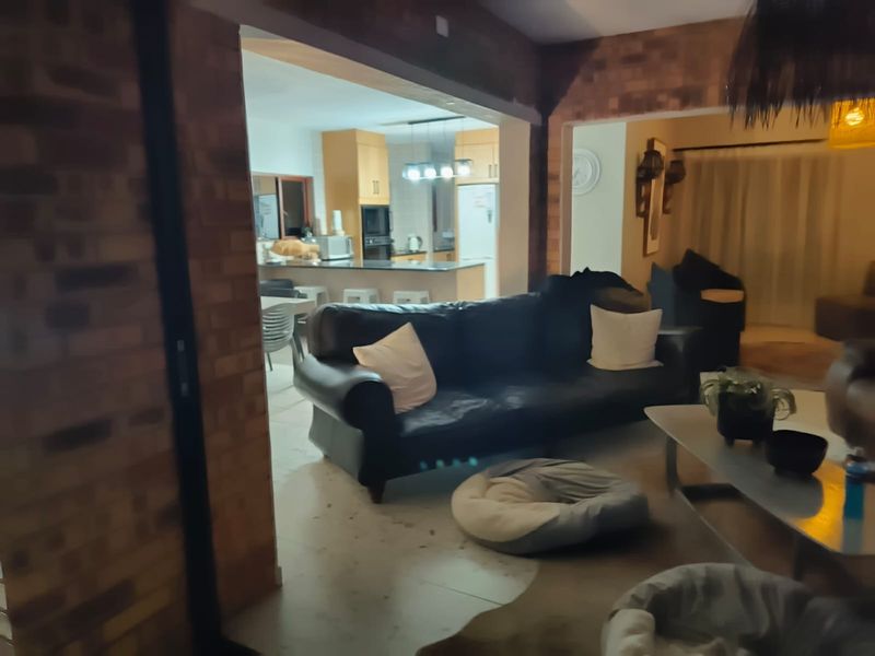 Open plan living area featuring exposed brick walls and tiled flooring, seamlessly connecting to a functional kitchen with built-in cabinetry and island.