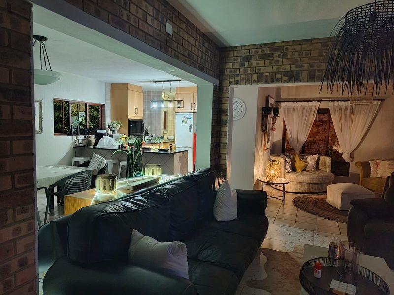 Open plan living area featuring exposed brick walls, tiled flooring, and a functional kitchen with island, creating a warm and connected living space.