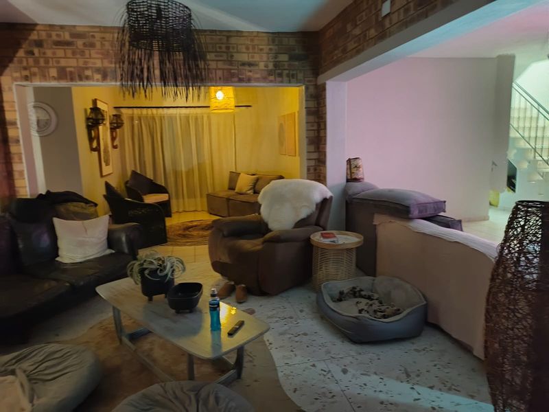 Spacious living area featuring exposed brick walls and terrazzo flooring, with an open-plan layout leading to an adjacent lounge space and staircase.