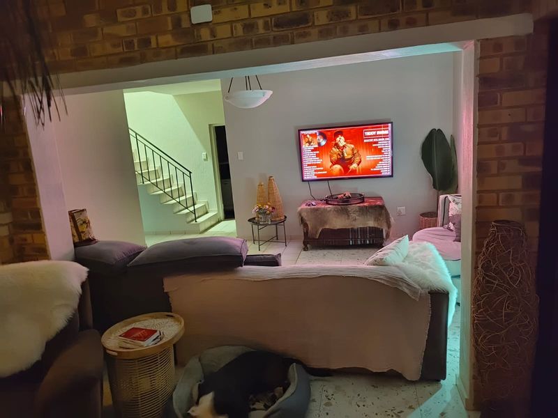 A living room area featuring exposed brick walls, tiled flooring, and an open-plan layout with a staircase leading to the upper level.