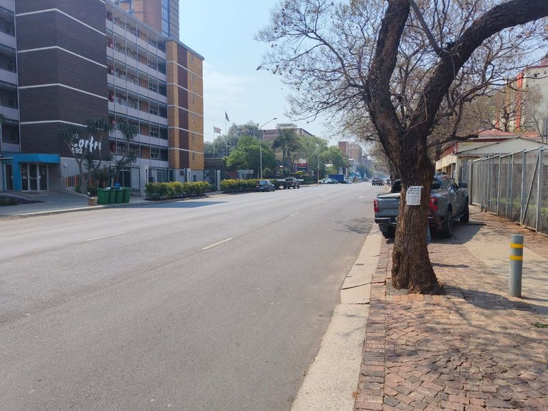 A street-level view showing the apartment building exterior, adjacent road, and paved sidewalk area.