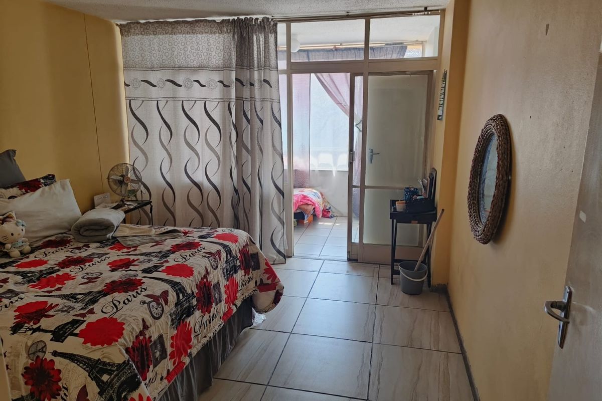 A bedroom featuring tiled flooring and direct access to an adjoining balcony through a glass door, offering potential for cosmetic updates.
