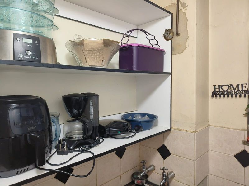 A kitchen area featuring built-in shelving and tiled splashback, showing visible signs of wall surface damage and peeling paint requiring maintenance.