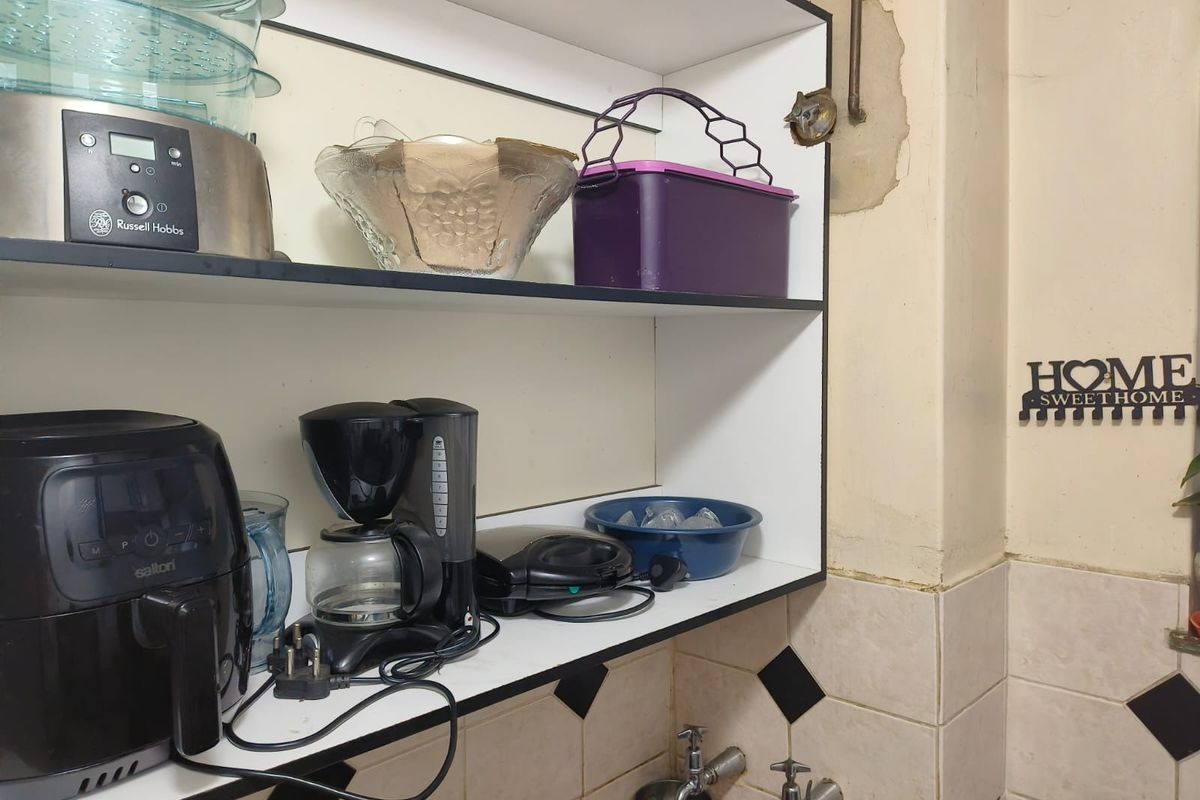 A kitchen area featuring built-in shelving and tiled splashback, showing visible signs of wall surface damage and peeling paint requiring maintenance.