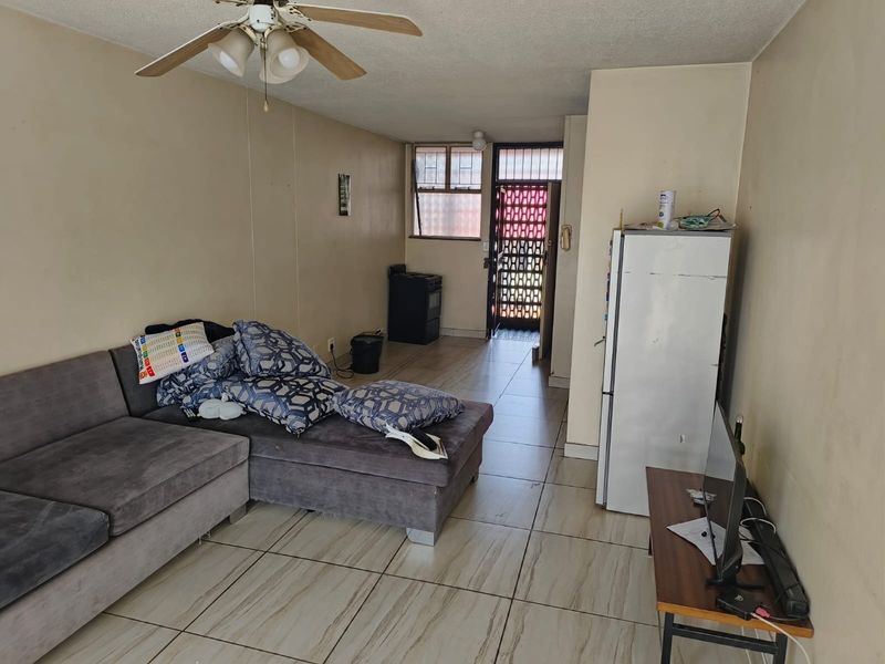 Open plan living area featuring tiled flooring, a ceiling fan, and direct access to a secure entrance door.