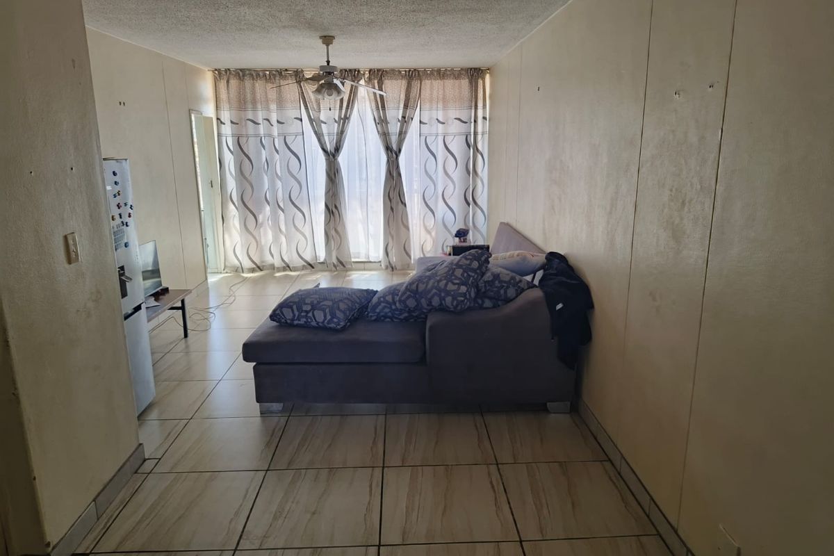 A living room area featuring tiled flooring, a ceiling fan, and a large sliding glass door providing natural light.