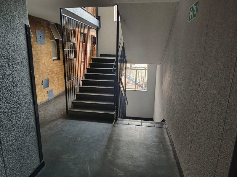 A functional apartment building stairwell featuring tiled flooring, brickwork accents, and metal security railings providing access between levels.