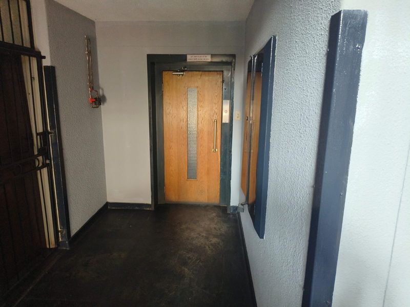 A functional apartment building hallway featuring an elevator access point, security gate, and textured wall finishes.