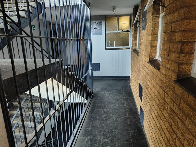 A communal apartment hallway featuring brick walls, tiled flooring, and a metal security gate leading to the staircase.