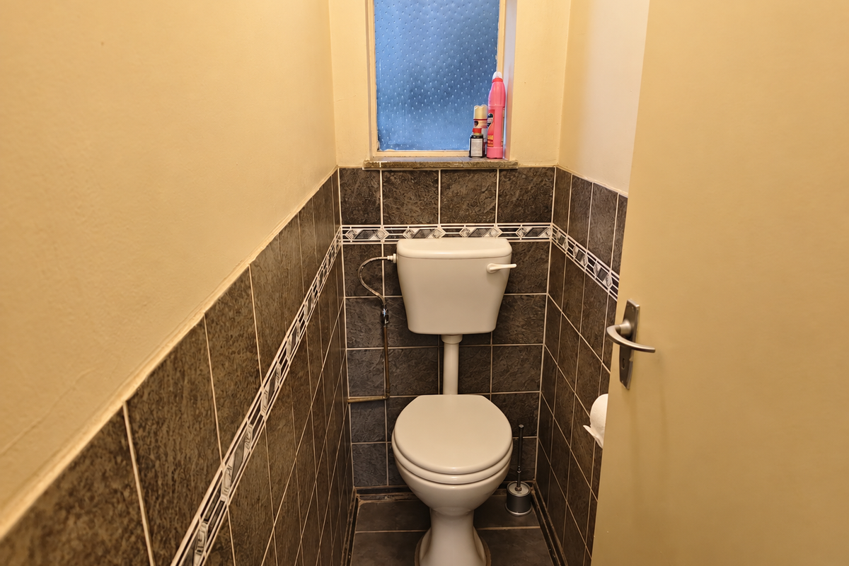 A compact guest toilet featuring dark ceramic wall and floor tiles with a decorative border and an obscured glass window for privacy.