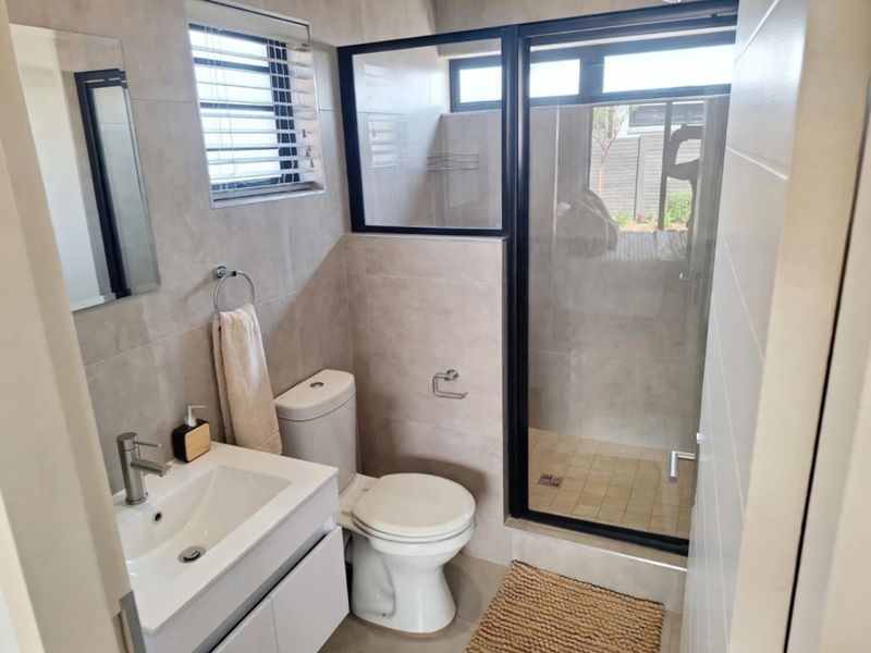 Modern bathroom featuring a sleek vanity, toilet, and a walk-in shower with a black-framed glass enclosure and neutral wall tiling.