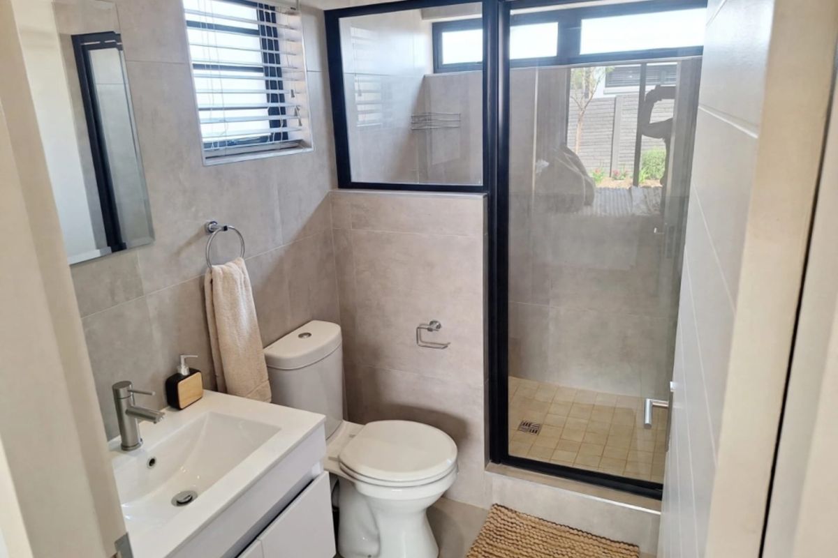 Modern bathroom featuring a sleek vanity, toilet, and a walk-in shower with a black-framed glass enclosure and neutral wall tiling.