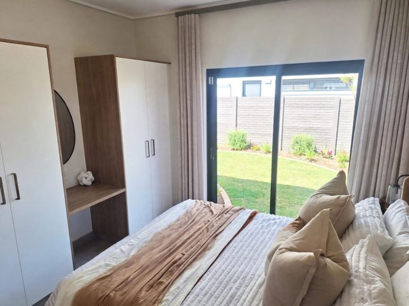A bright bedroom featuring built-in cupboards with a vanity area and a large sliding glass door providing direct access to the rear garden.