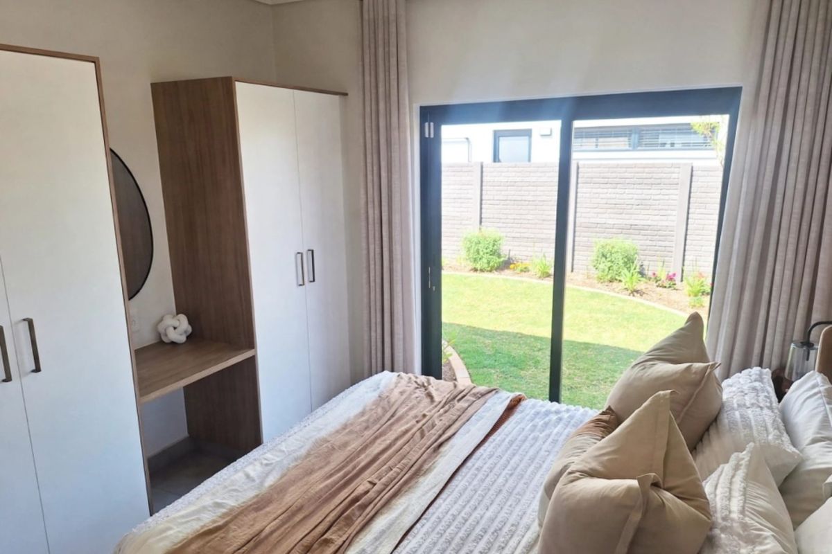 A bright bedroom featuring built-in cupboards with a vanity area and a large sliding glass door providing direct access to the rear garden.