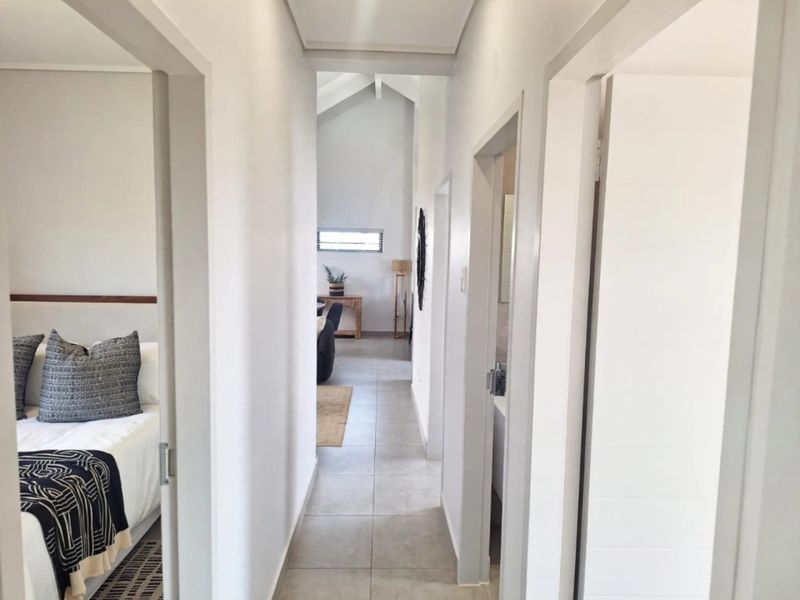 A bright, neutral hallway with tiled flooring and vaulted ceilings, providing access to adjacent bedrooms and living areas.