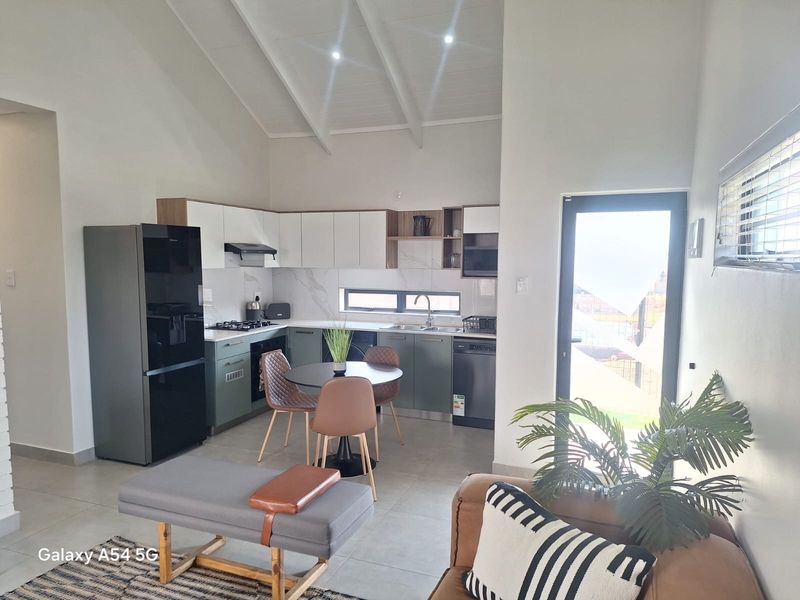 Modern open-plan kitchen and living area featuring vaulted ceilings, contemporary cabinetry, integrated appliances, and direct access to the outdoor space.