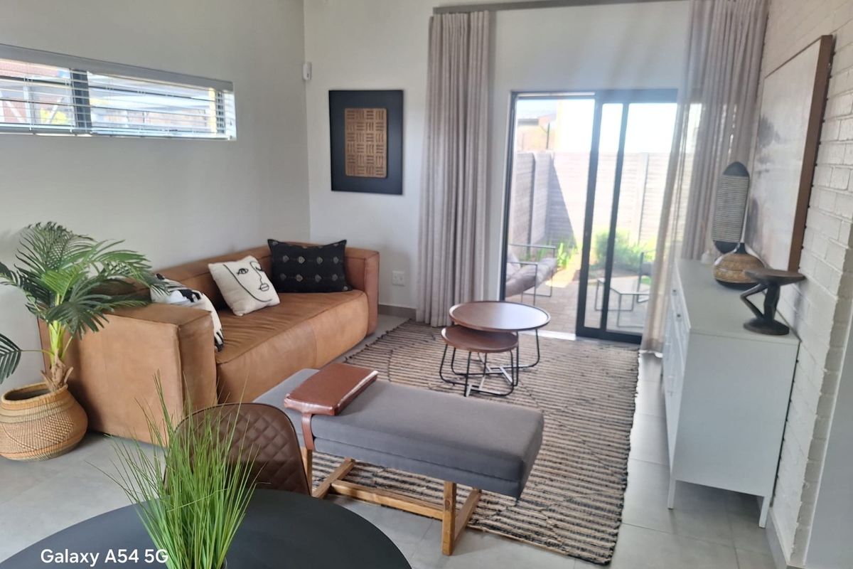 Bright living room featuring tiled floors, exposed beam ceilings, and large sliding glass doors providing direct access to the rear patio area.