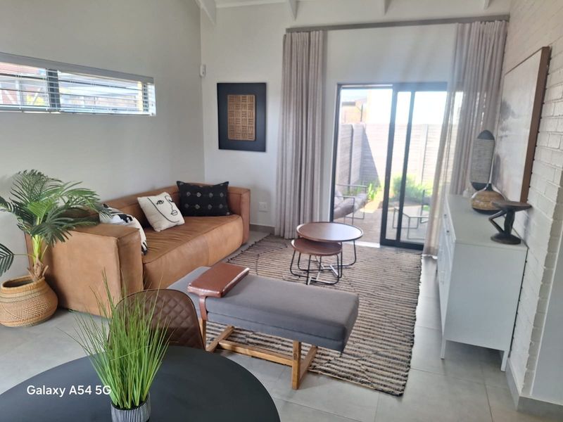 Bright living room featuring tiled floors, exposed beam ceilings, and large sliding glass doors providing direct access to the rear patio area.