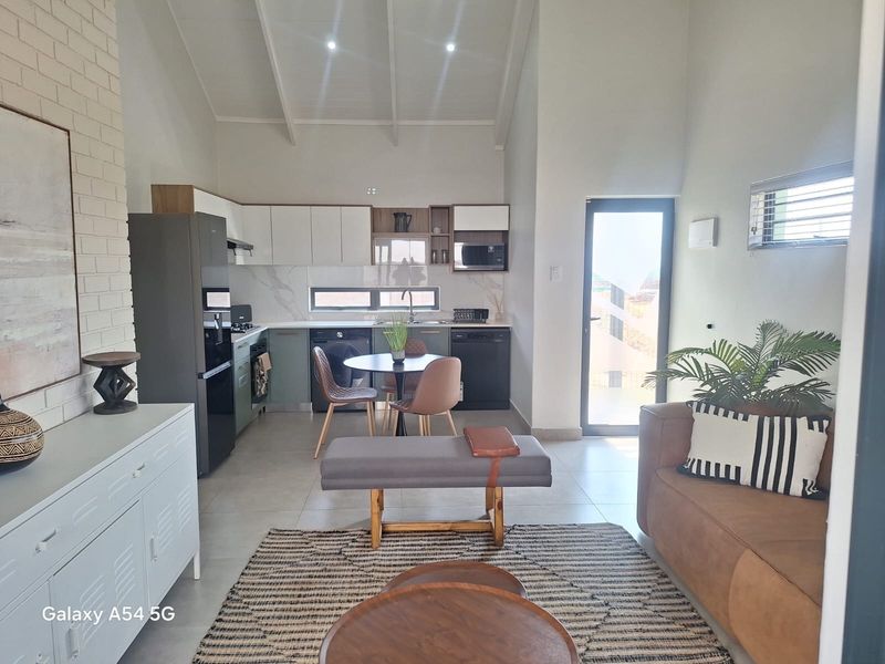 Modern open-plan living area featuring a contemporary kitchen with built-in cabinetry, vaulted ceilings, and tiled flooring, seamlessly connecting to the living space.