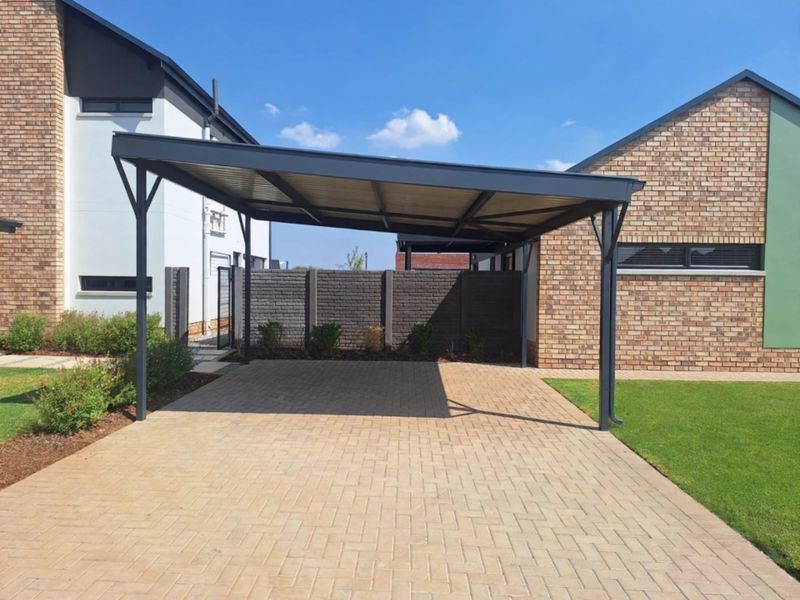 A modern, well-maintained carport structure providing covered parking, situated on a paved driveway with surrounding brick boundary walls and landscaped garden areas.