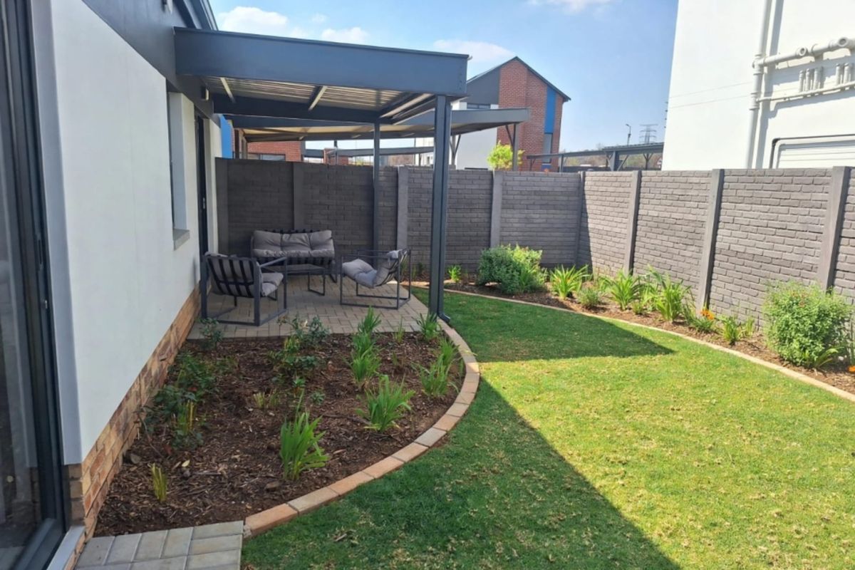 A well-maintained rear garden featuring a covered patio area, paved pathways, and a neat lawn enclosed by a brick boundary wall.