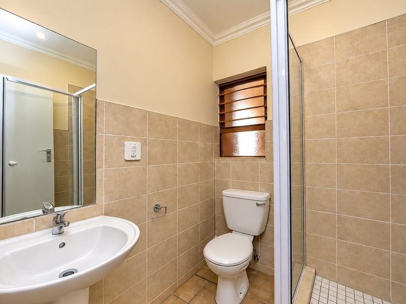 A clean, functional bathroom featuring a pedestal basin, toilet, and a glass-enclosed shower with neutral wall and floor tiling.
