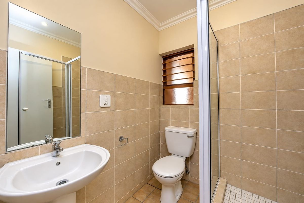 A clean, functional bathroom featuring a pedestal basin, toilet, and a glass-enclosed shower with neutral wall and floor tiling.