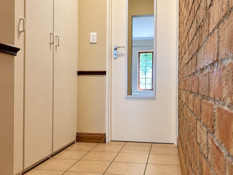 A clean, well-maintained hallway featuring tiled flooring, built-in storage cupboards, and a distinctive exposed brick feature wall.