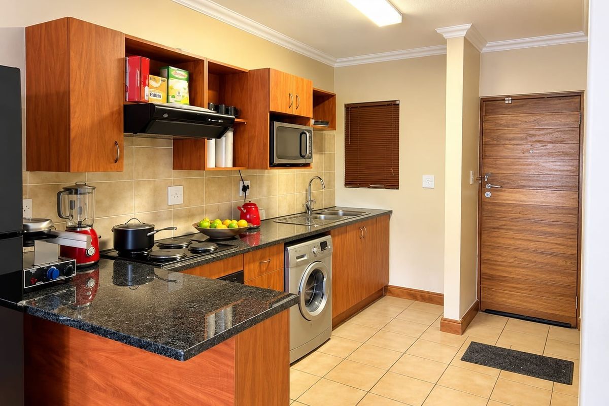 A functional kitchen featuring wood-finish cabinetry, granite countertops, integrated appliances, and tiled flooring, with direct access to the main entrance door.