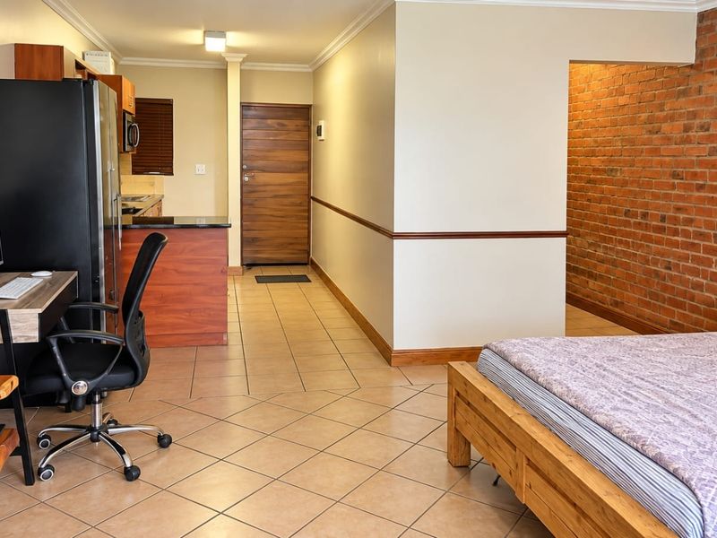 Open-plan studio apartment featuring tiled flooring, an exposed brick feature wall, and a compact kitchen area with granite countertops.