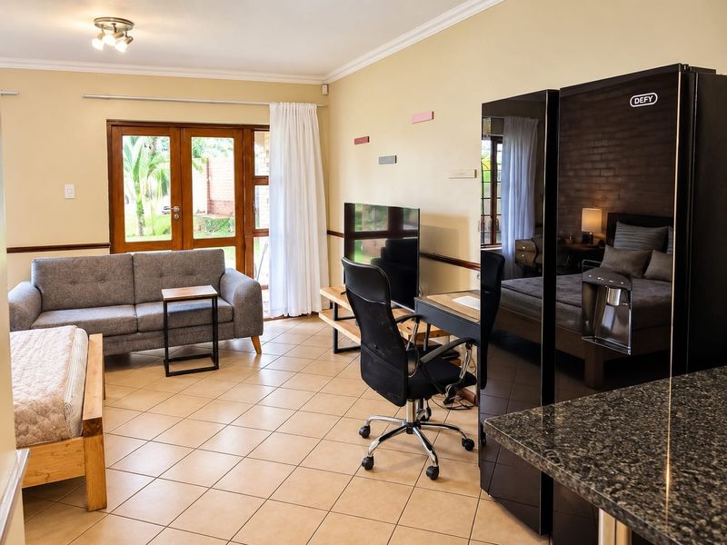Open-plan living area featuring tiled flooring, granite kitchen counter, and direct access to the garden through wooden framed glass doors.