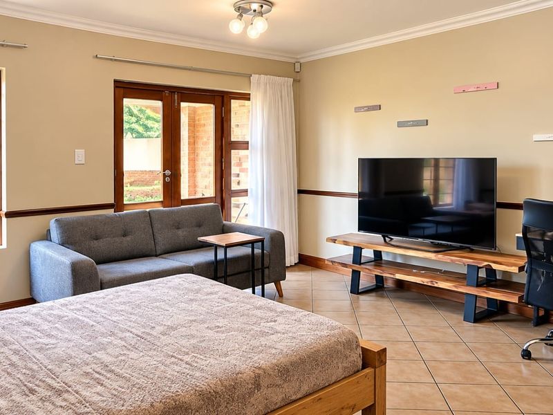 Spacious bedroom featuring tiled flooring, large windows with security bars, and direct access to an outdoor area through wooden doors.