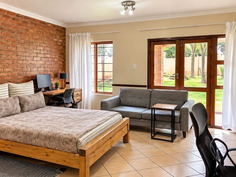 Spacious bedroom featuring an exposed brick feature wall, tiled flooring, and direct access to the garden through double glass doors.