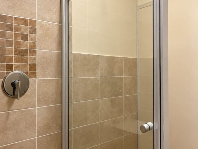 A clean, modern shower stall featuring neutral-toned wall and floor tiles, a glass enclosure, and a chrome shower mixer.