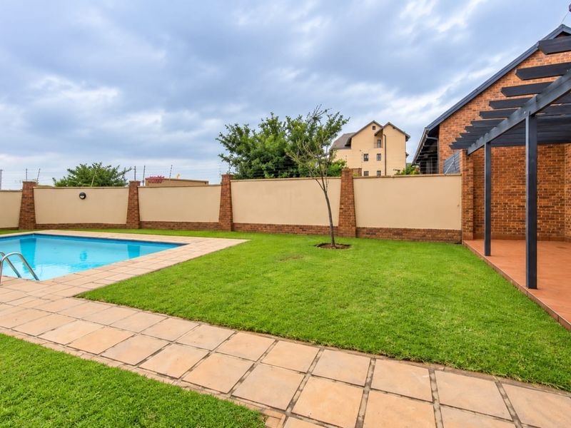 A well-maintained outdoor area featuring a swimming pool, a covered pergola patio, and a landscaped lawn enclosed by a secure boundary wall.